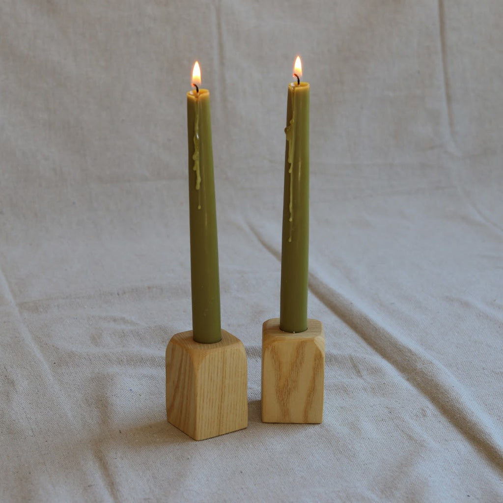 Two green candles in wooden holders on a beige fabric background