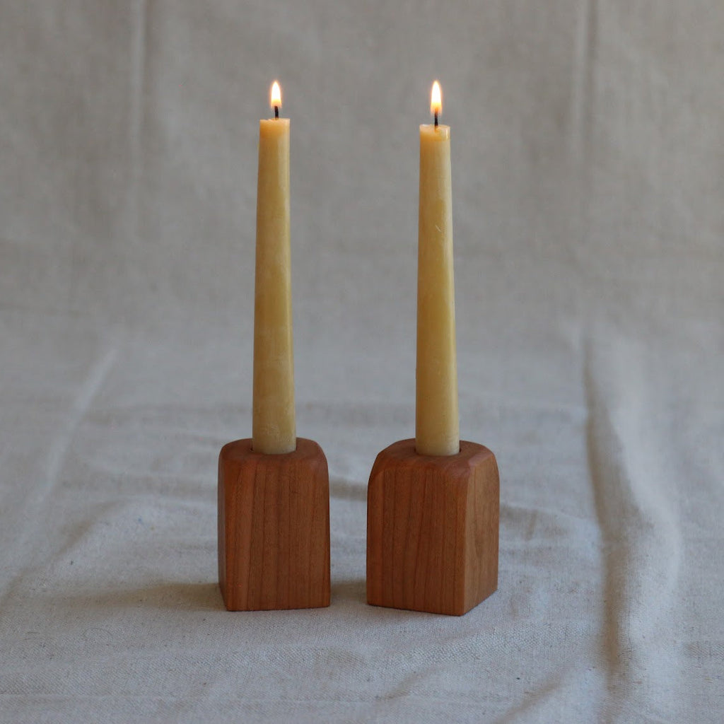 Two lit candles in wooden holders on a plain background