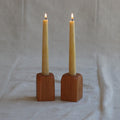 Two lit candles in wooden holders on a plain background